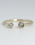 A gold ring with a single round opal gemstone and a smaller diamond on the opposite side.