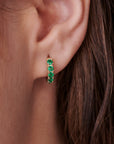 Gold hoop earrings with a row of green emerald gemstones.