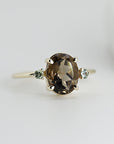 A gold ring with a large oval-shaped brown gemstone and two smaller green gemstones on either side.
