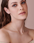 A gold chain necklace with three small round stones hanging from it. The necklace is worn by a person with long brown hair.