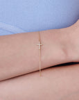 Diamond cross bracelet in 14k gold with a sideways design, shown on a woman’s wrist for scale and styling as minimalist Christian jewelry.