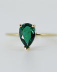 A gold ring with a pear-shaped emerald green gemstone.