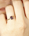 A gold ring with a rectangular, dark purple gemstone