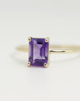 A gold ring with a purple emerald-cut amethyst gemstone.
