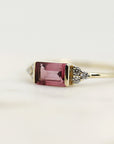 A gold ring with a rectangular pink gemstone and small diamonds on the band.