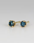 A pair of gold stud earrings with blue round sapphire gemstones.