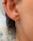 Gold hoop earrings with a dangling emerald green rectangular emerald stone.