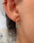 Gold hoop earrings with a dangling emerald green rectangular emerald stone.