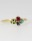 A gold ring with a cluster of five gemstones. The stones are red, green, blue, and green. The ring is set with small gold beads around the stones.