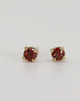 A pair of gold stud earrings with small, round, red gemstones.