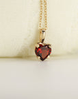 A gold necklace with a heart-shaped garnet pendant featuring a red gemstone.