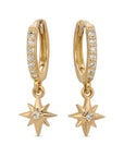 A pair of gold hoop earrings with a dangling star charm. Each hoop is adorned with a row of small, clear diamond stones. The star charms have a single clear diamond stone in the center.