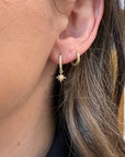 A gold hoop earring with a small star charm dangling from it. The star charm is set with small diamonds.