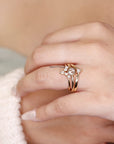 A gold ring set with a round center stone and smaller pear-shaped stones. The ring is set on a band with two thinner bands underneath.