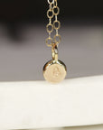 A gold chain necklace with a small, round pendant featuring the letter &