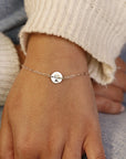 A silver chain bracelet with a small round charm featuring a tree design.