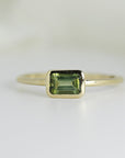 A gold ring with a green emerald-cut green tourmaline gemstone.