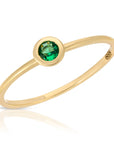 A delicate gold ring with a single round green emerald gemstone set in a bezel setting.