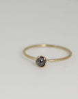 A simple gold band ring with a single black diamond gemstone.