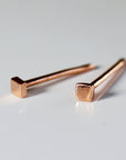 Two rose gold square stud earrings on a white surface.