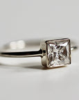 A gold moissanite ring with a square-shaped clear gemstone.