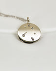 A gold necklace with a round pendant featuring a constellation of small diamonds