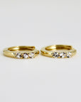 A pair of gold hoop earrings with three small clear diamonds set in each hoop.
