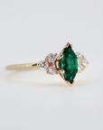 14k Gold Marquise Emerald Ring with Diamond Accents. A gold ring with a marquise-shaped emerald green gemstone surrounded by smaller clear gemstones.