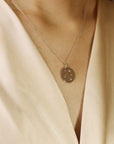 A white gold necklace with a round pendant featuring a constellation design with small clear diamond stones.