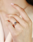 A gold ring set with a blue gemstone and smaller clear gemstones. The ring is worn on a person&