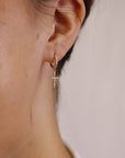 Gold hoop earrings with a dangling cross charm, both adorned with small clear cubic zirconia stones.
