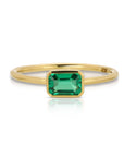 A gold ring with a green emerald gemstone set in a bezel setting.