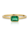 A gold ring with a green emerald gemstone set in a bezel setting.