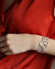A silver bracelet with a delicate, intricate design featuring a floral pattern. The bracelet is adorned with small, colorful gemstones in shades of red, green, and blue.