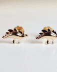 A pair of gold-toned dinosaur stud earrings. The dinosaurs are facing to the right and have a spiky back.