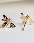 A pair of gold bee stud earrings with diamond accents. The bee is facing to the right with its wings spread out. The earrings are on a white background.