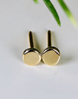 A pair of gold stud earrings with round, flat tops.