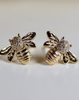 A pair of gold bee stud earrings with diamond accents. The bees are facing opposite directions.