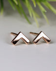 A pair of rose gold chevron stud earrings. The earrings are small and simple, with a geometric design.