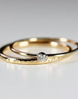 Two gold rings, one with a hammered texture, are stacked together. A single, small, round diamond is set in the top ring.