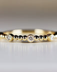 A delicate gold ring featuring a series of small, evenly spaced beads. Three larger, bezel-set diamonds are interspersed among the beads. The ring has a polished, shiny finish, and is set against a soft, neutral background.