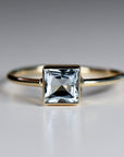A gold ring with a square-shaped aquamarine gemstone.