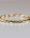A thin gold band ring with a braided design.