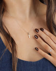 A delicate gold chain necklace with a small, rectangular pendant featuring a single diamond. The necklace is worn by a person with brown hair and dark brown nail polish.