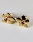 A pair of gold flower-shaped earrings with a red garnet gemstone in the center of each flower.