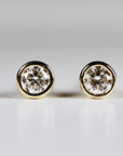 A pair of gold stud earrings with round, clear diamond gemstones.