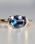 East-west oval lab sapphire engagement ring set in a half bezel 14k gold solitaire design, displayed on a white background.