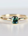 A gold ring with a square-shaped, bezel-set, teal blue montana sapphire gemstone.