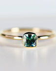 A gold ring with a square-shaped, bezel-set, teal blue montana sapphire gemstone.
