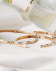 Three gold bracelets with engraved messages. The top bracelet reads "I love you forever". The middle bracelet reads "Emma" with a heart symbol and the date "03.14.2024". The bottom bracelet has a floral design.